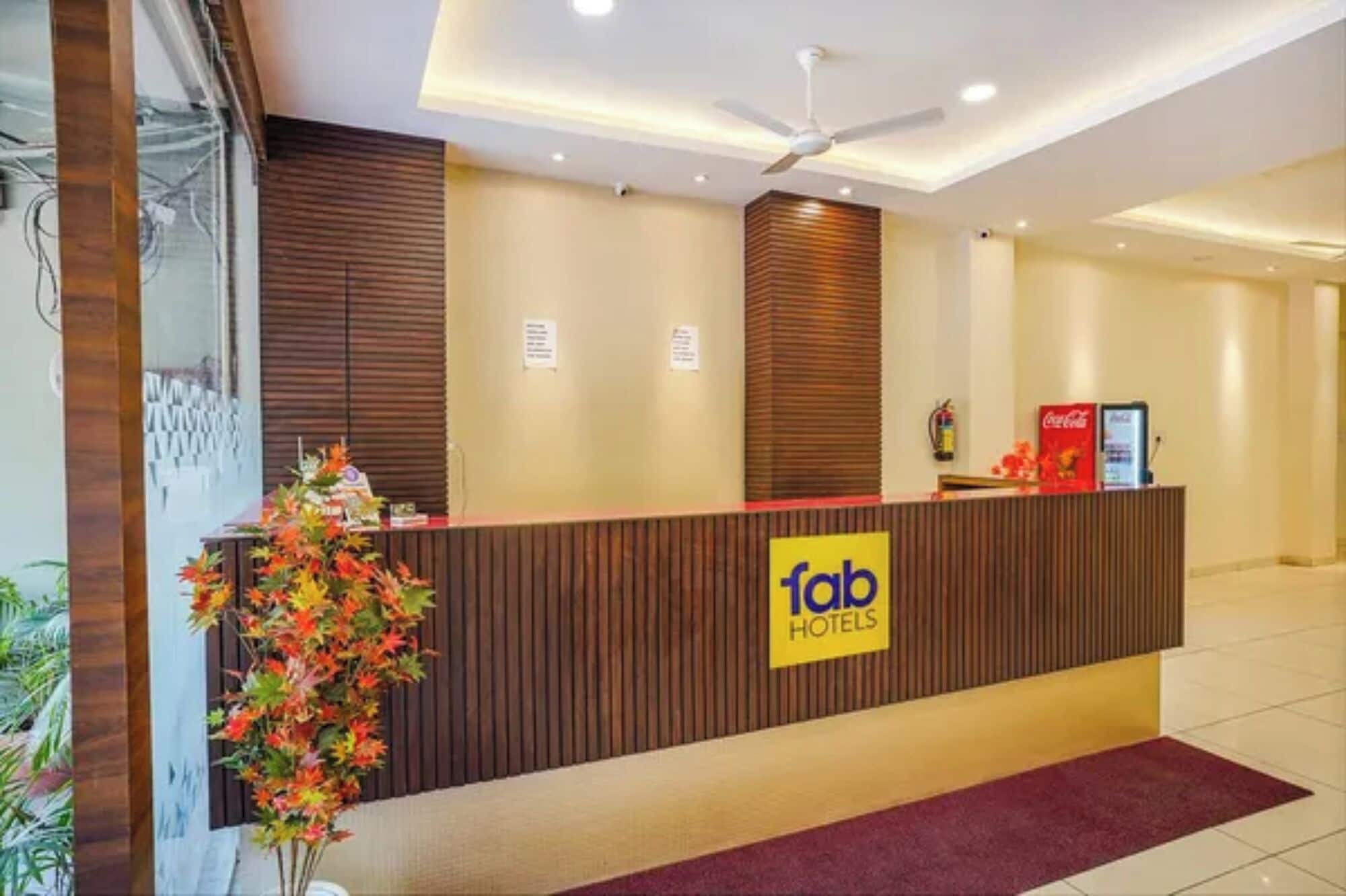 Ein Hotelrezeptionstresen mit Holzvertäfelung, ein Schild mit der Aufschrift 'fab hotels', eine Coca-Cola-Maschine und ein Deckenventilator.