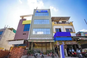 Un hotel de varios pisos con un letrero que dice 'Hotel Sukh Vilas' y 'Tab Hotels' sobre la entrada.