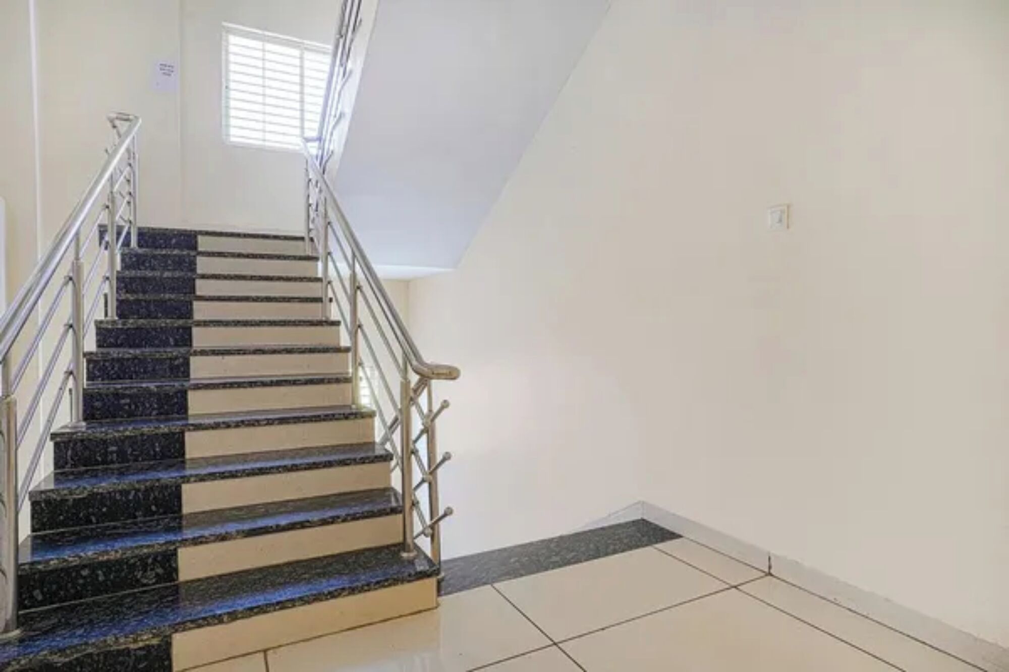 Eine Treppe mit Metallgeländern und Fliesenboden, die zu einer Zwischenebene führt.