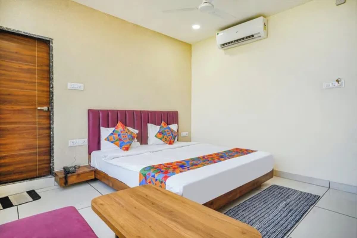 Una habitación de hotel con una cama, un banco de madera, un equipo de aire acondicionado y una puerta.