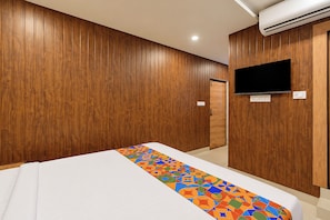 A hotel room with wooden panel walls, a bed with a colorful geometric-patterned bed runner, a flat-screen TV mounted on the wall, and an air conditioning unit above it. - FabHotel Priya Residency (Hyderabad)