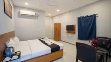 Una habitación de hotel con cama, escritorio, silla, televisión, armario y cortina.