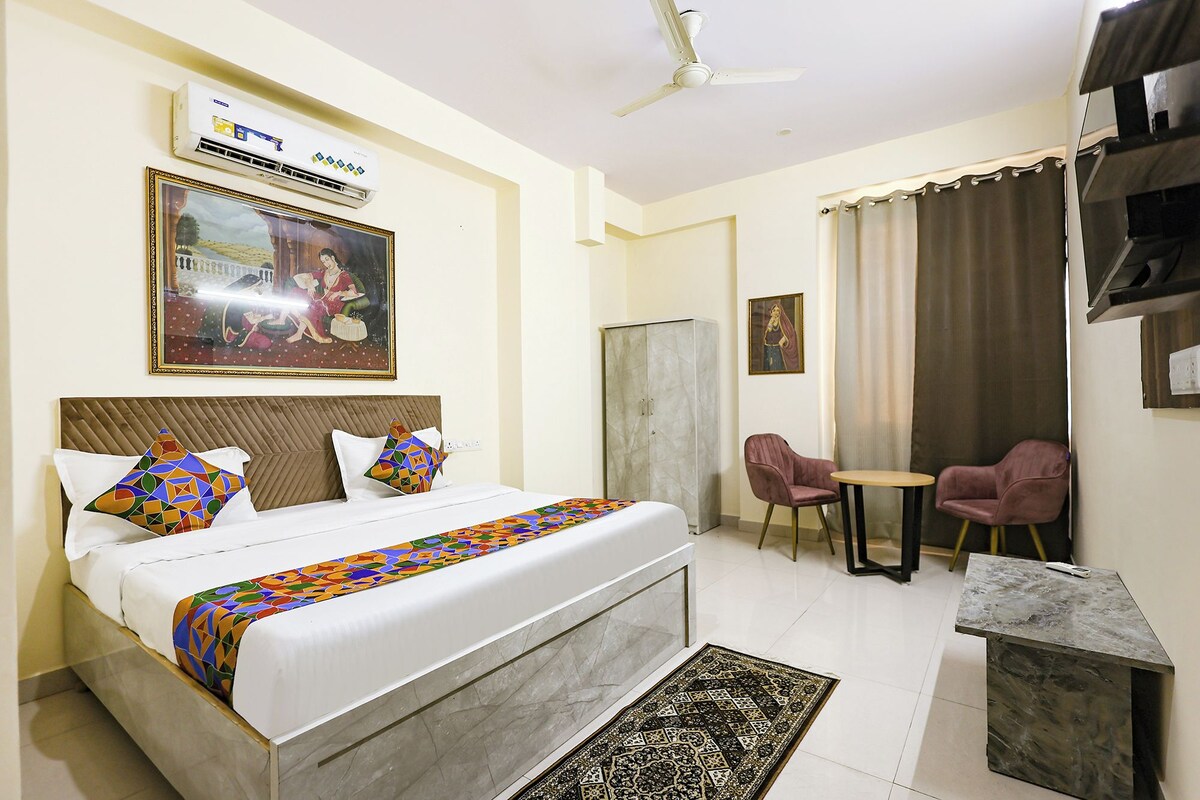 Une chambre d’hôtel avec un lit, un bureau, deux chaises, un ventilateur de plafond, un appareil de climatisation et un tableau au mur.