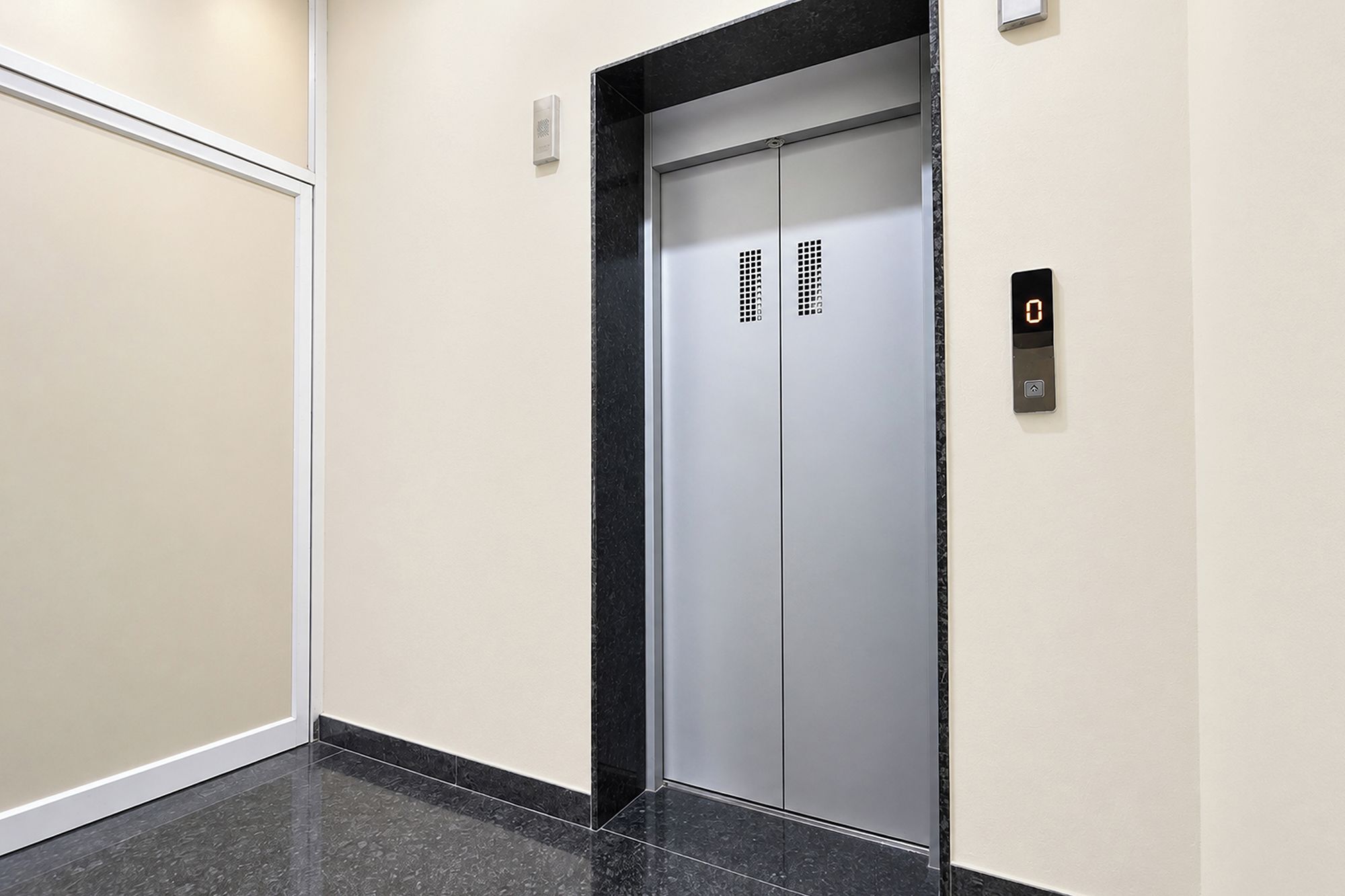 A modern elevator with a digital display, a control panel, and a door with ventilation grilles.