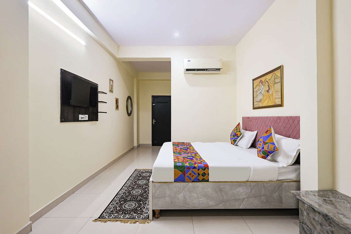Habitación de hotel con cama, televisión montada en la pared, una puerta y un cuadro.