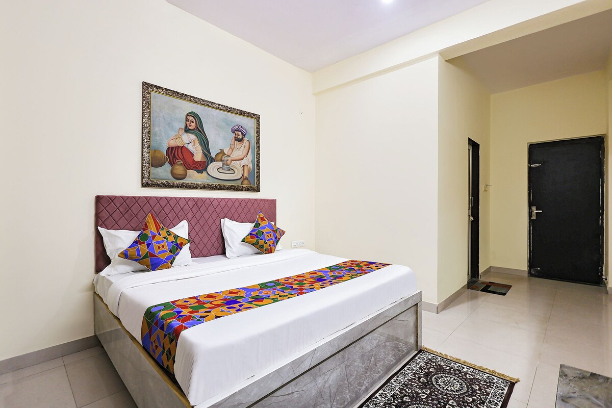 A hotel room with a bed, pillows, a painting, a door, and a patterned rug.