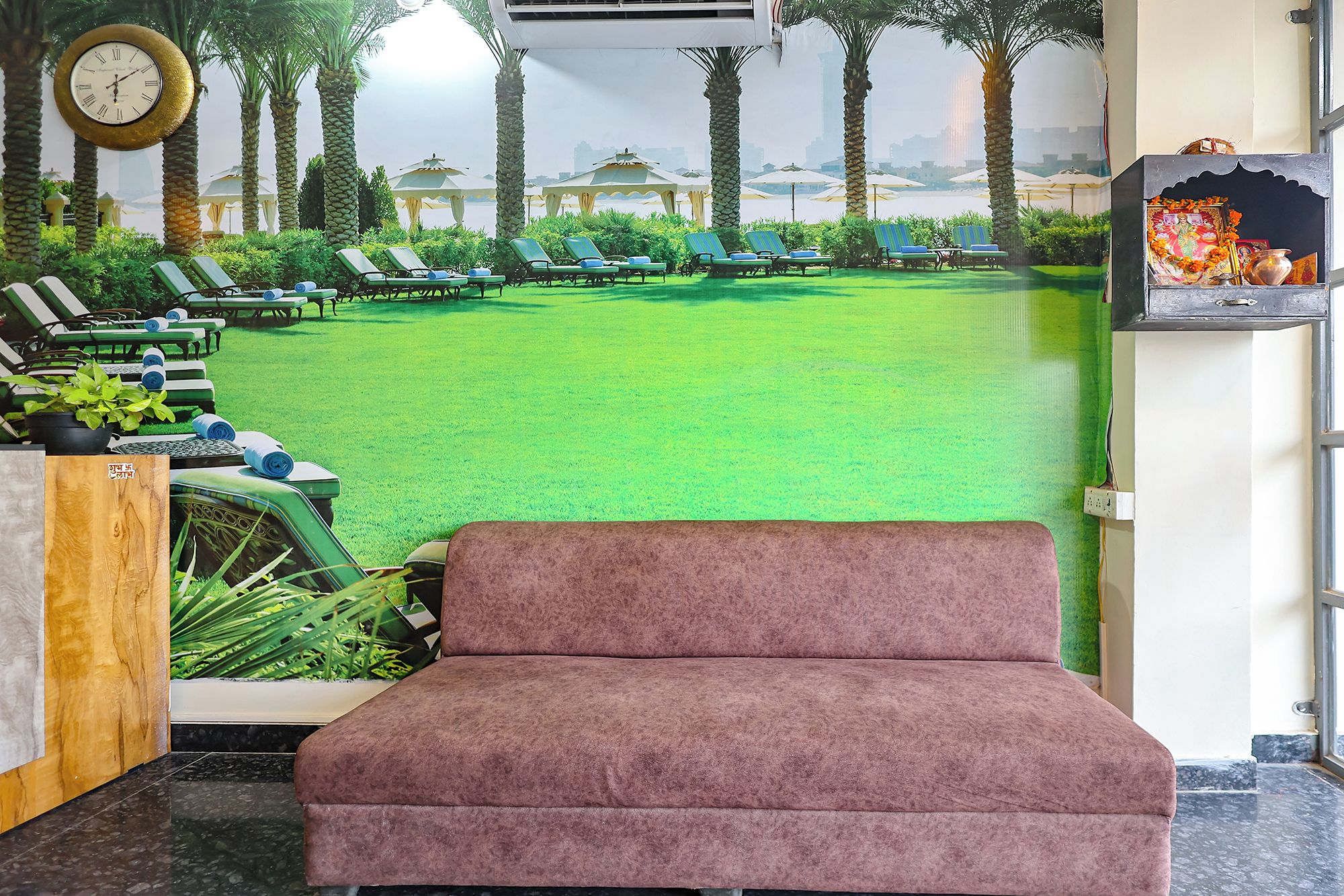 Un área de recepción con césped artificial verde, sillones de descanso y un reloj en la pared.