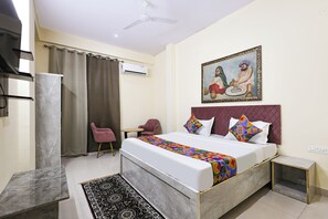 A hotel room with a bed, a desk, a chair, a ceiling fan, and a painting on the wall. - Fabhotel Vaishali Inn (Jaipur)
