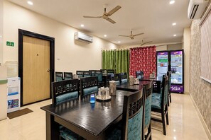 A hotel dining area with a long table, multiple chairs, ceiling fans, an air conditioning unit, and a water dispenser.