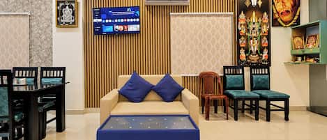 A modern living room with a sofa, ottoman, and chairs. There is a flat-screen TV mounted on the wall, and decorative wall panels.