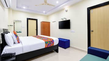 A hotel room with a bed, a television, a wardrobe, and a desk with a telephone.