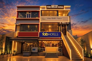 Un hotel de varios pisos con un letrero destacado que dice 'The Hills Aura' y un letrero de 'fabHOTELS'.