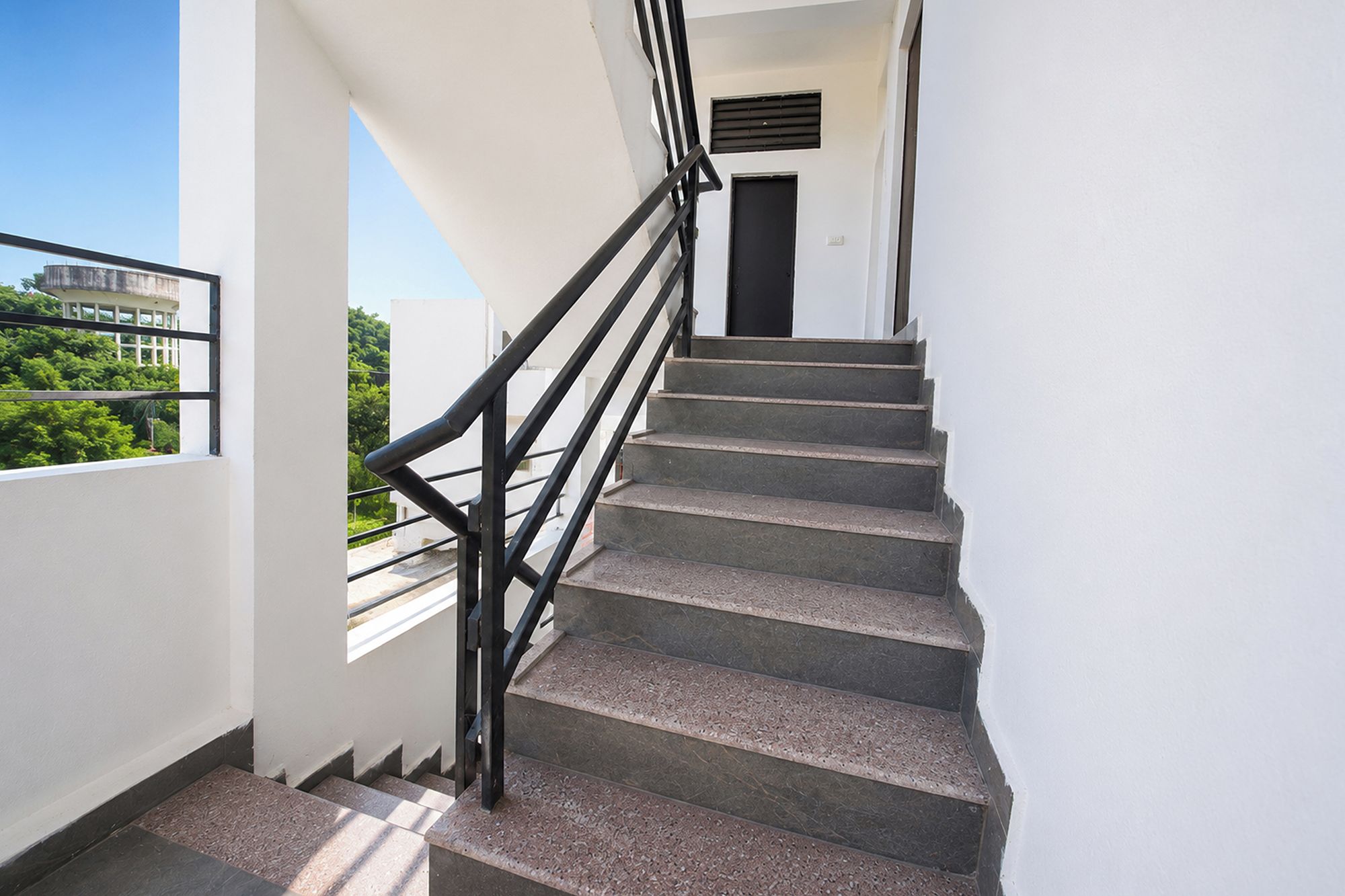 Eine Treppe mit schwarzer Handlauf, die zu einer Tür oben führt.