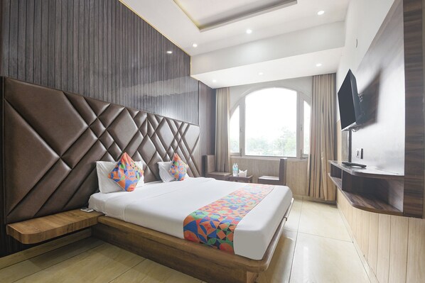 Una habitación de hotel moderna con una cama grande, un televisor montado en la pared y una ventana con cortinas.