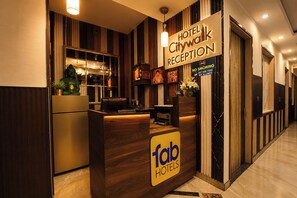Zona de recepción de un hotel con mostrador, una estatua de Buda y un cartel con el nombre del hotel y recepción.