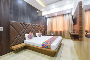 Habitación de hotel con una cama grande, un cabecero de madera, una mesita de noche y un televisor montado en la pared.