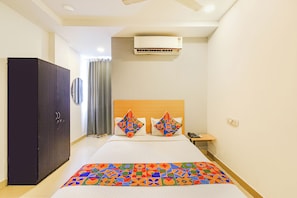 A hotel room with a bed, a wardrobe, an air conditioning unit, a bedside table with a phone, and a wall-mounted mirror. - FabHotel The Luxor - Nr Rajiv Gandhi International Cricket Stadium, Uppal (Hyderabad)