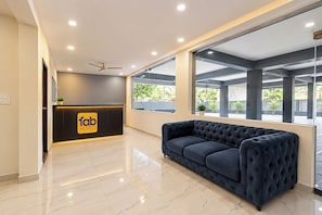 A hotel reception area with a reception desk, a ceiling fan, and a large window offering a view of the outdoors.