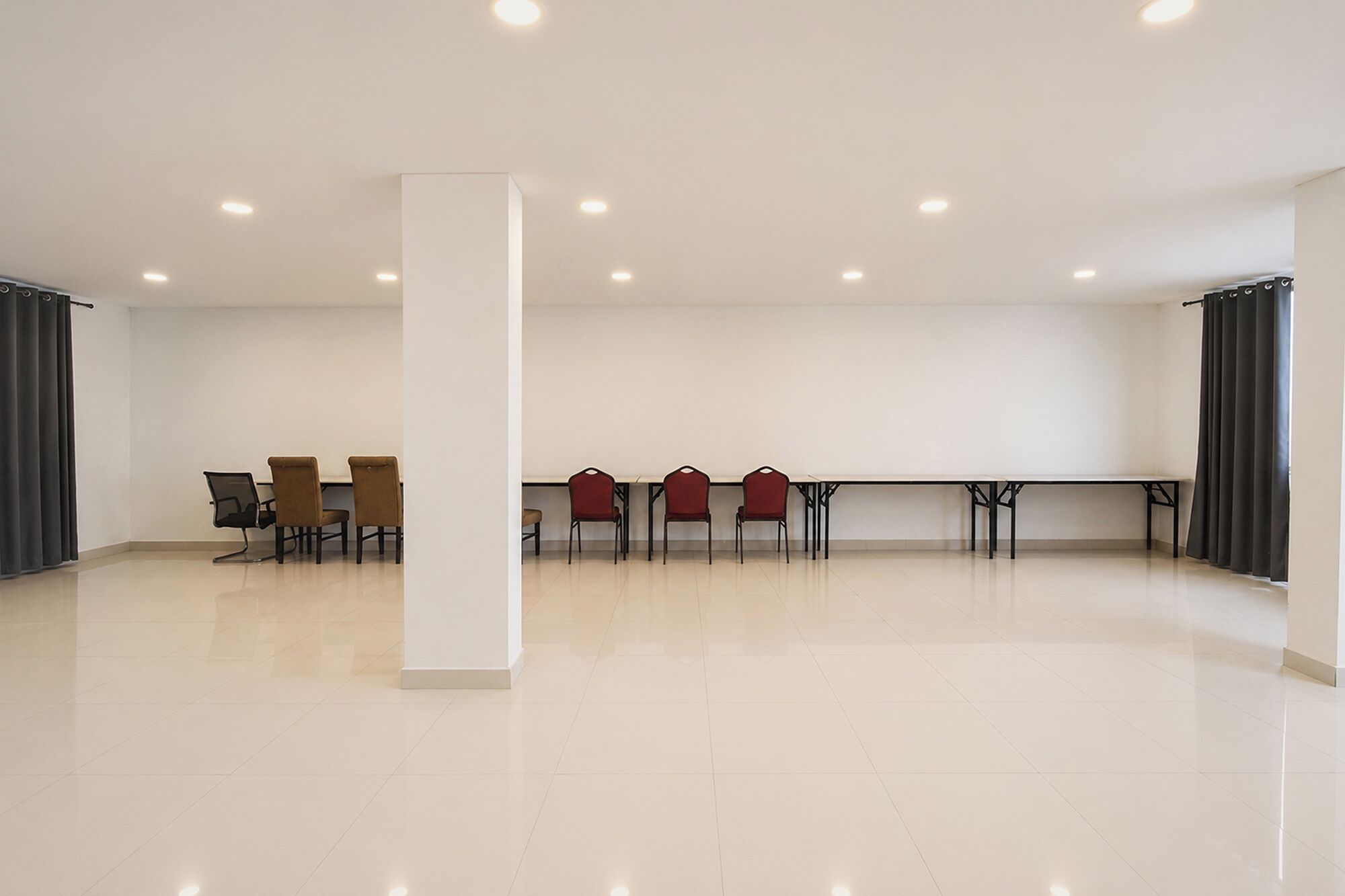 A spacious room with a high ceiling, recessed lighting, a central pillar, and a row of chairs along one wall.