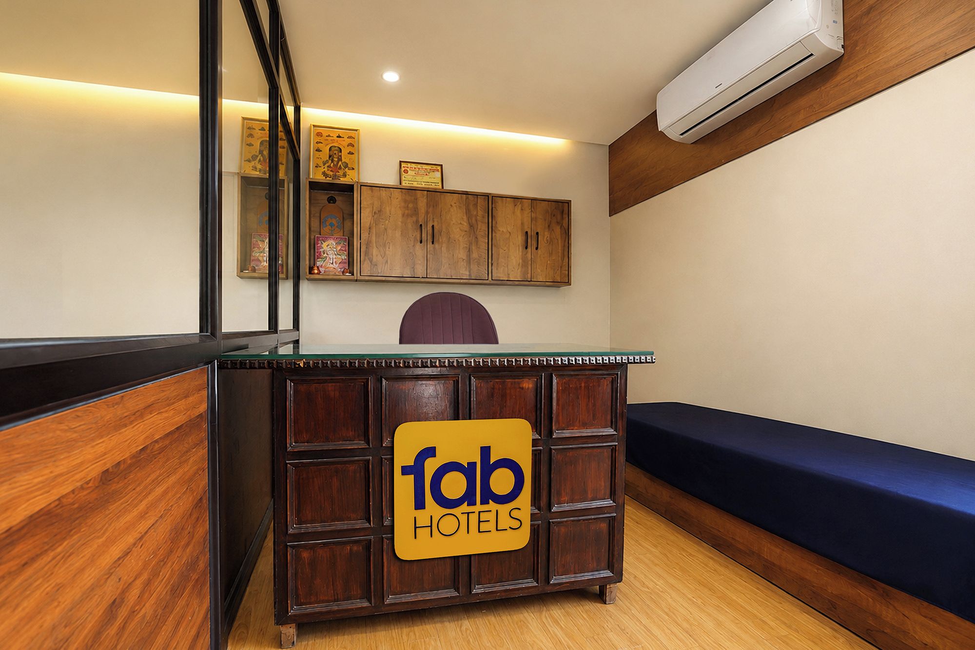 Un comptoir d’accueil avec une enseigne indiquant « fab hotels », des meubles en bois, un canapé bleu et un appareil de climatisation.