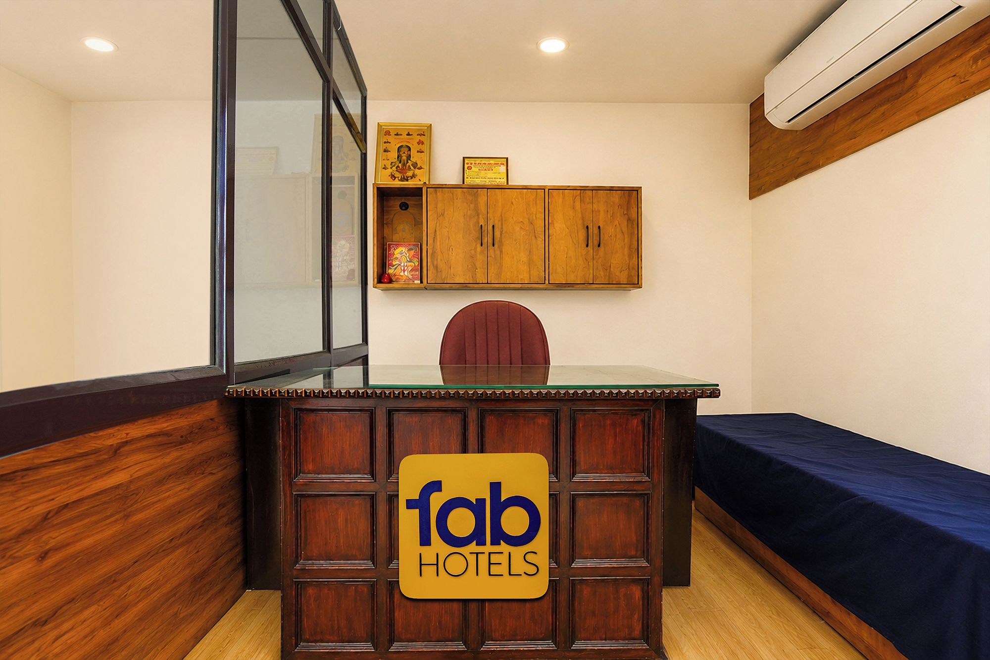 Habitación de hotel con escritorio de madera, una silla, una cama con colcha azul y un mueble de pared con iconos religiosos.