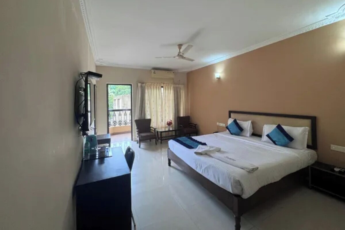A hotel room with a bed, a desk, a chair, a table, and a balcony with curtains.