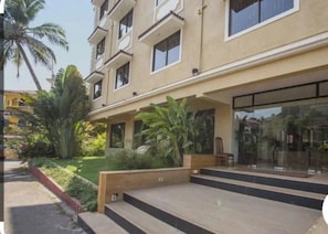 A multi-story building with a flat roof, a covered entrance area with steps, and a glass facade. - Oriva Rendezvous Beach Resort (Panaji)