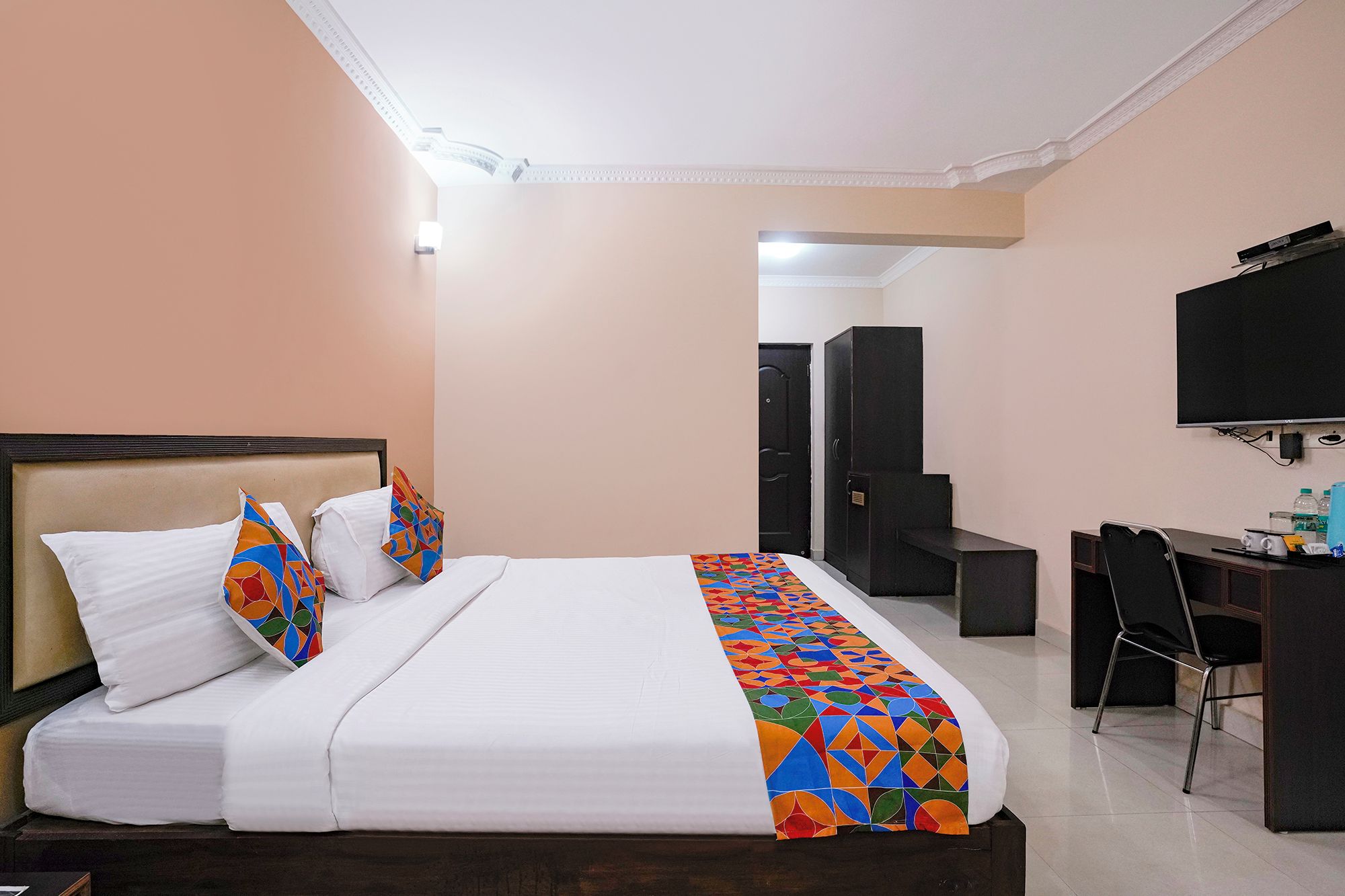 Habitació d'hotel amb llit, escriptori, cadira, armari i televisió.