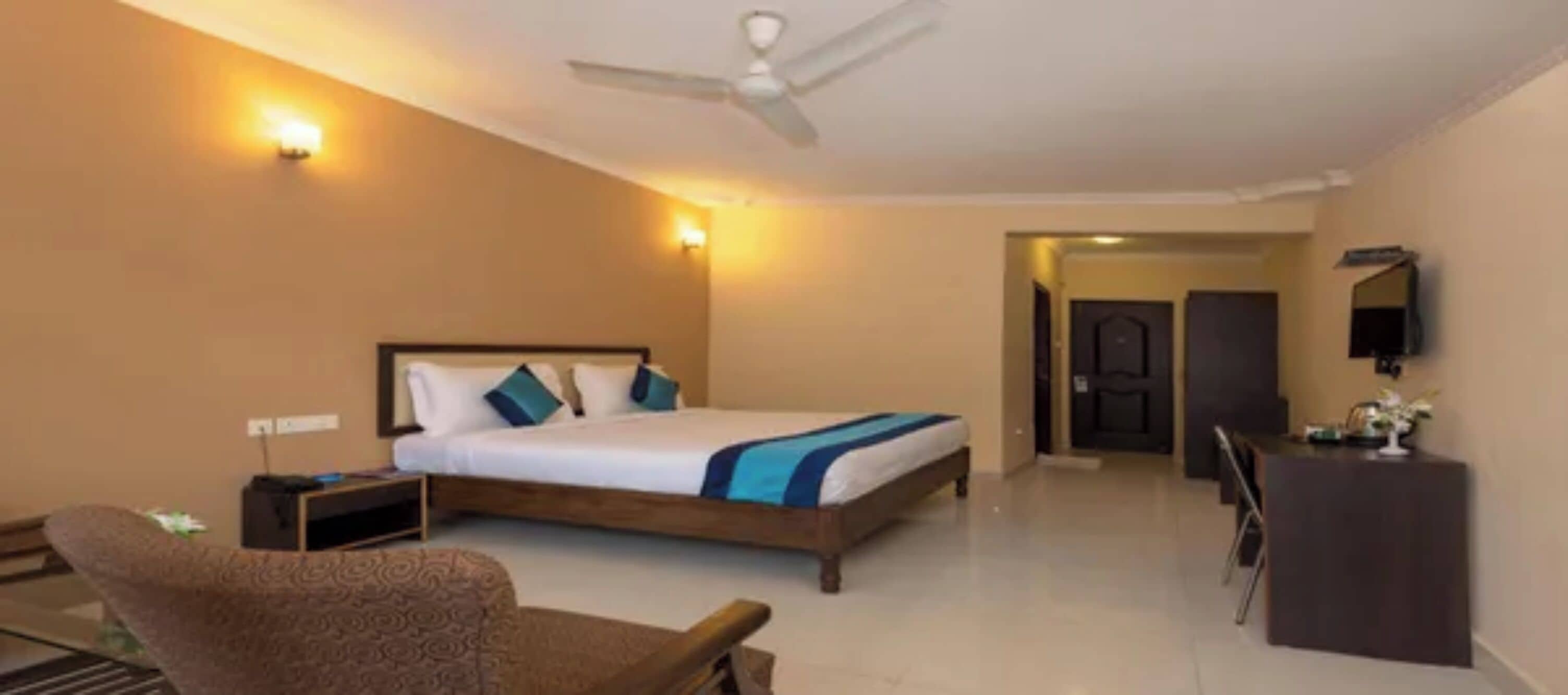 Habitación de hotel con cama, escritorio, silla, ventilador de techo y puerta que da a otra habitación.