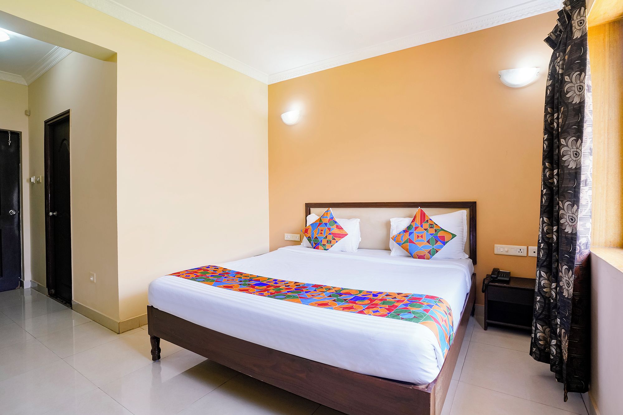 Una habitación de hotel con una cama grande, una mesita de noche, una lámpara y una cortina.