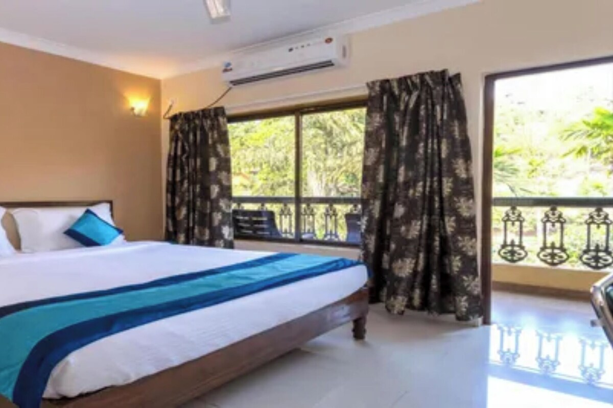 A hotel room with a bed, a nightstand, a window with curtains, and an air conditioning unit.
