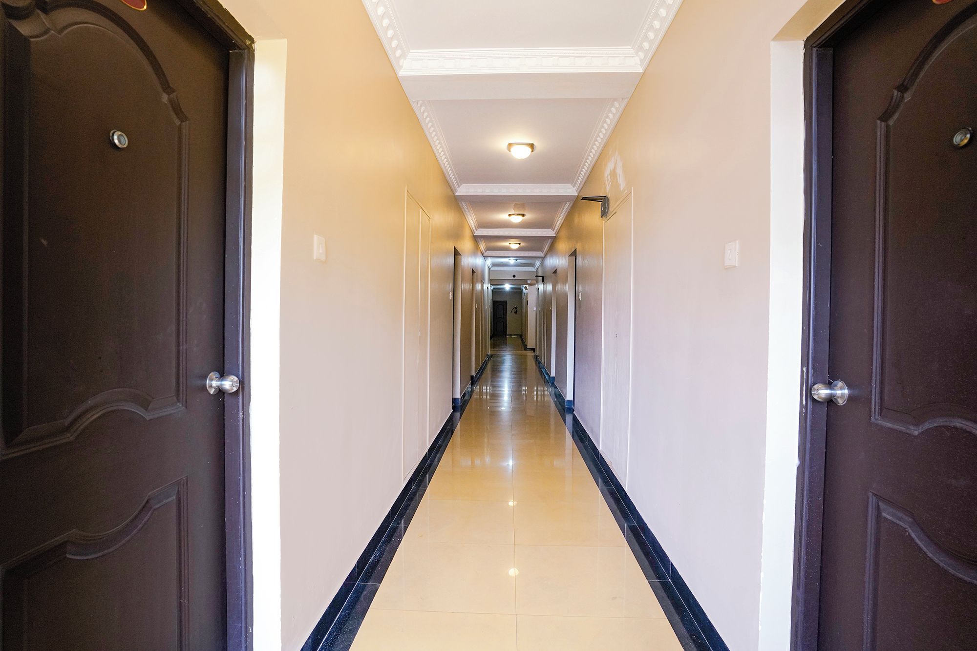 Un pasillo largo y estrecho con puertas de madera oscura a cada lado y piso de baldosas.