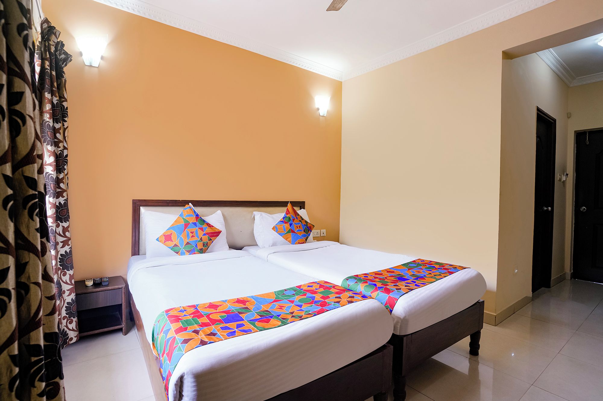 A double bed with a colorful geometric-patterned bedspread, a wooden headboard, and a nightstand with a remote control.