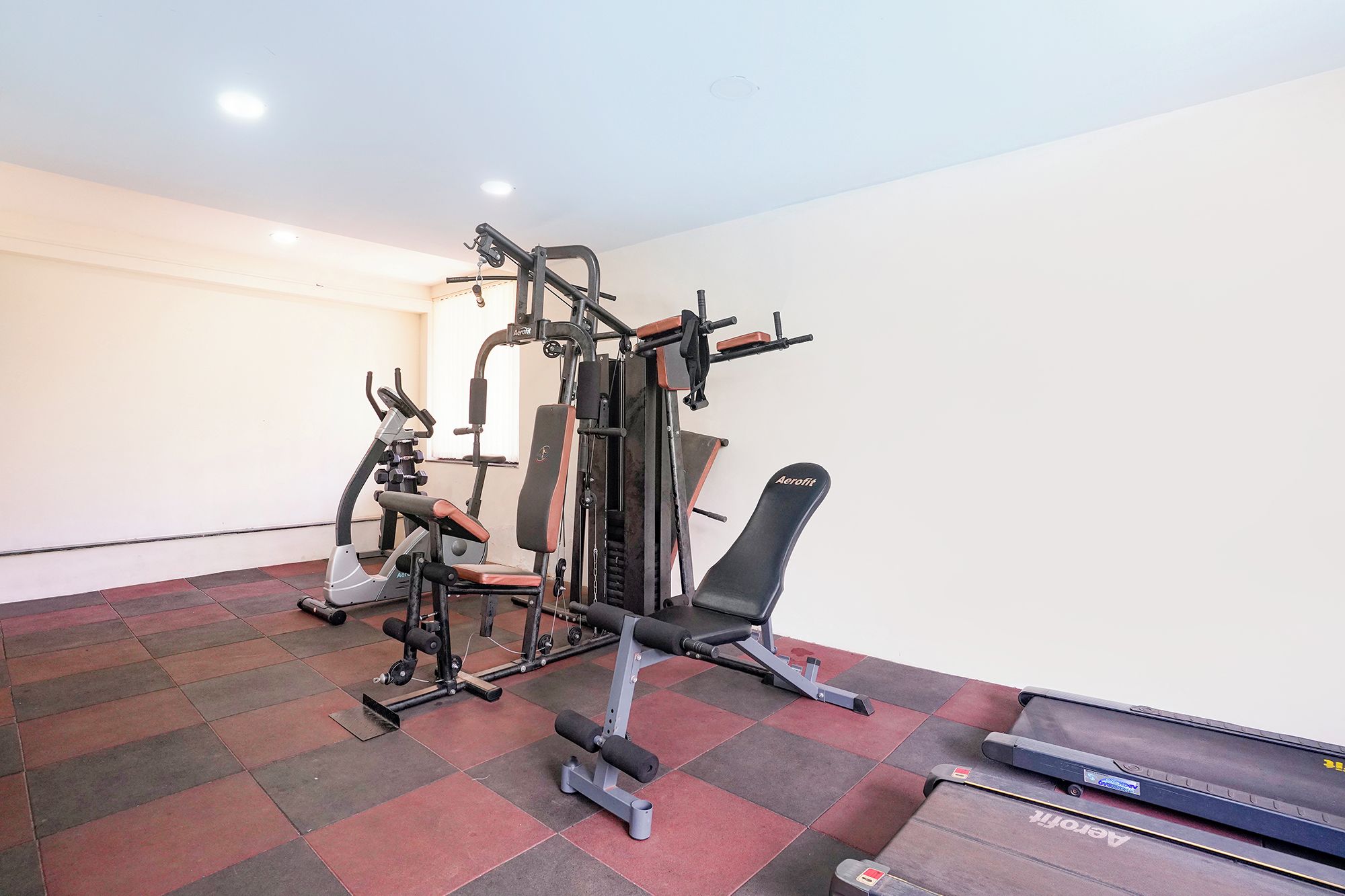 Ein Fitnessraum mit Trainingsgeräten, einer Bank und einem Laufband.