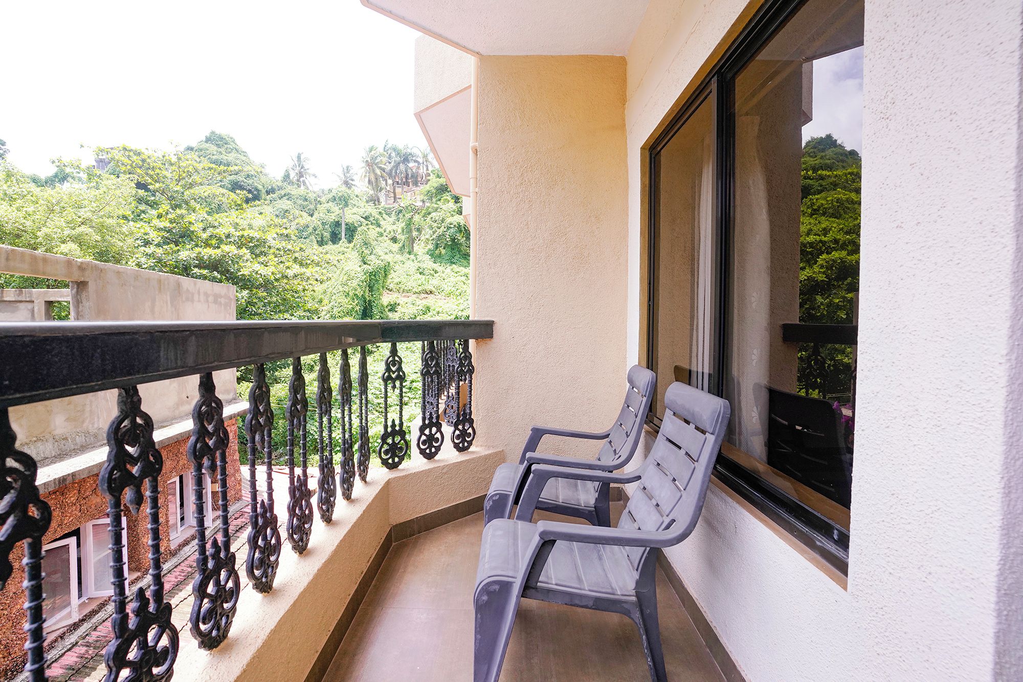 A balcony with a metal railing, a bench, and a window overlooking a green landscape.