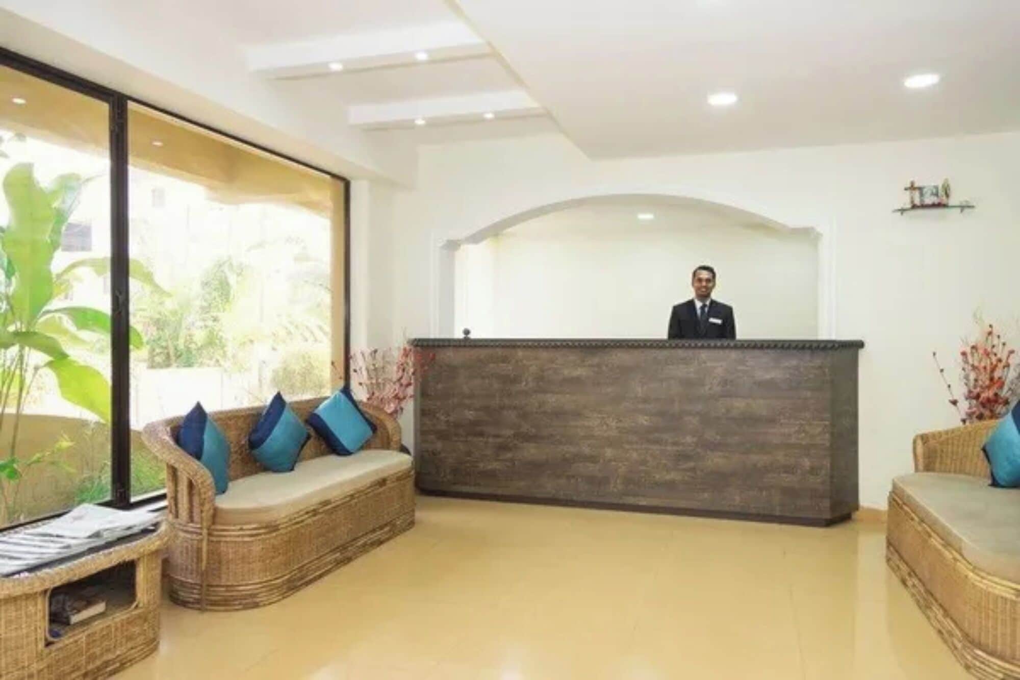 Una zona de recepción con mostrador de madera, mobiliario de mimbre y un amplio ventanal con vegetación al exterior.
