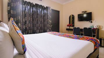 A hotel room with a bed, a television, a desk with chairs, and a window with curtains.