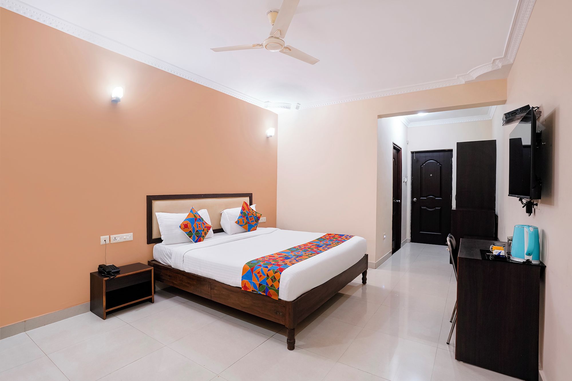 A hotel room with a bed, bedside table, nightstand, and a desk with a chair.
