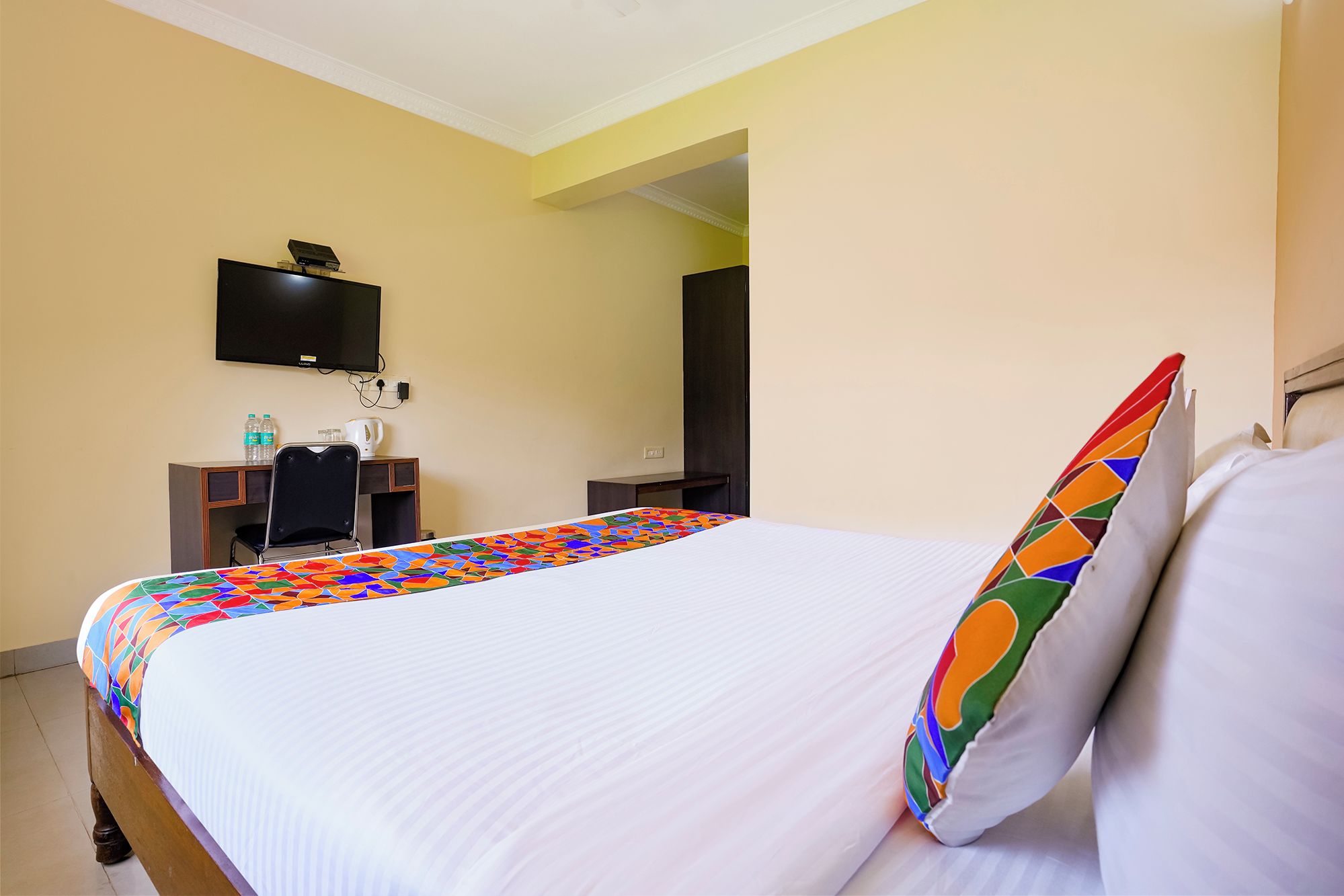 Habitación de hotel con cama, escritorio, silla, televisor y dispensador de agua.