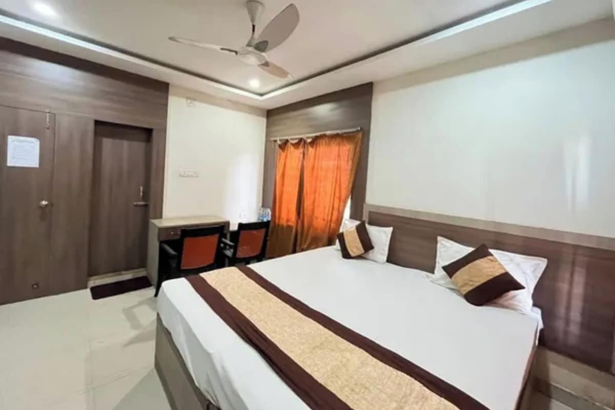 Una habitación de hotel con cama, escritorio, silla, armario y ventilador de techo.