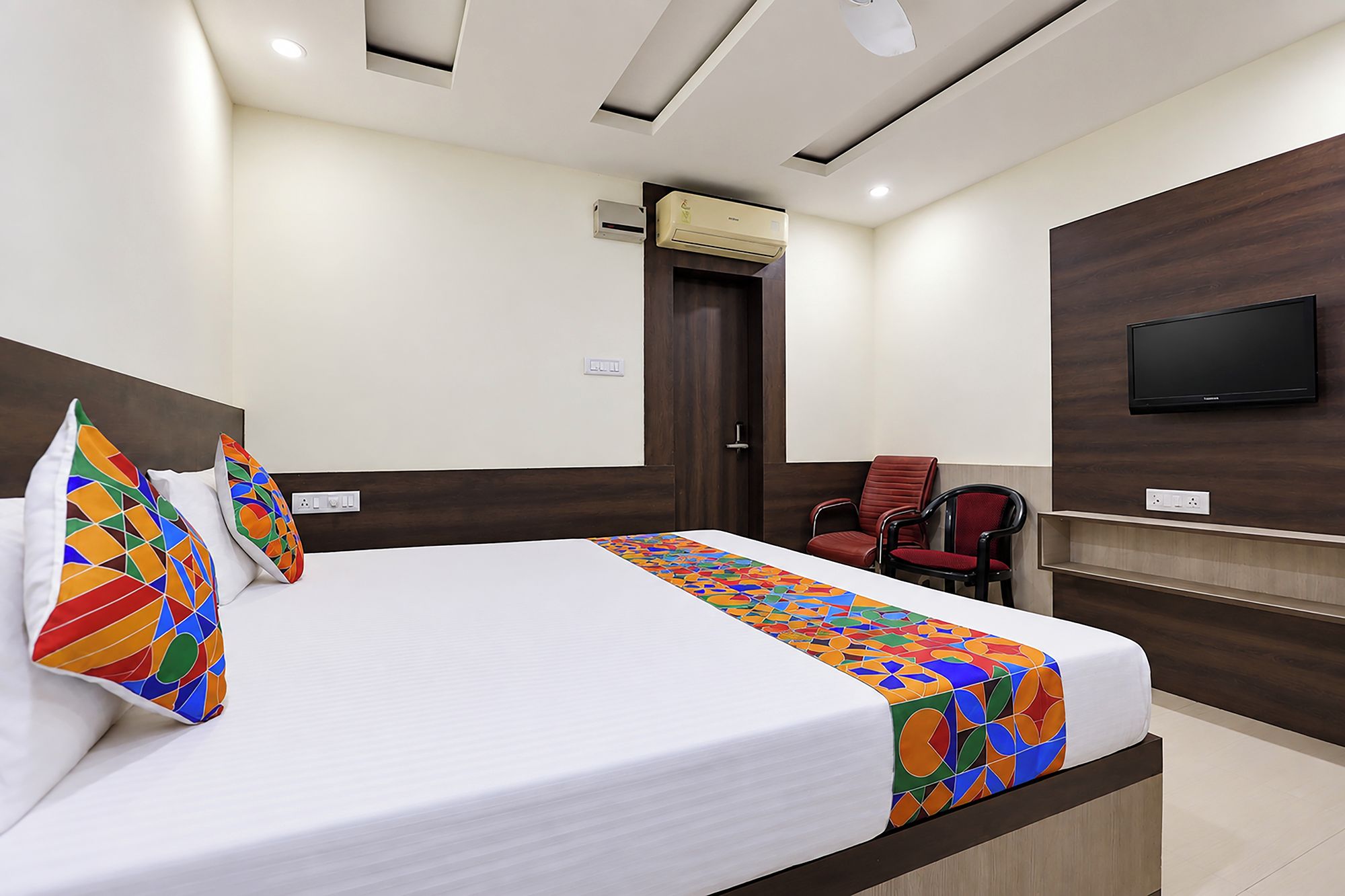 Una habitación de hotel con una cama, televisión, sillón y aire acondicionado.