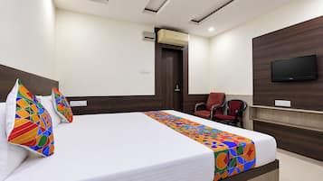 Una habitación de hotel con una cama, televisión, sillón y aire acondicionado.