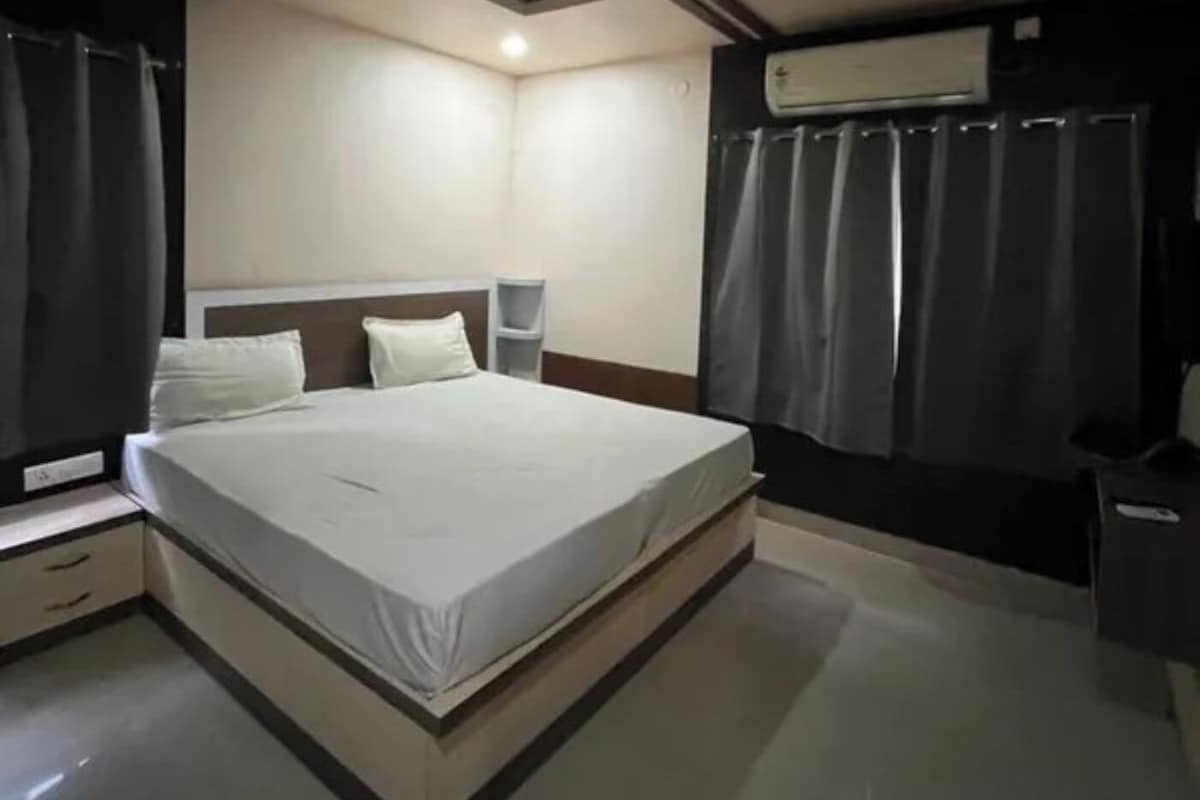 Una habitación de hotel con una cama, un ventilador de techo, un equipo de aire acondicionado y cortinas.