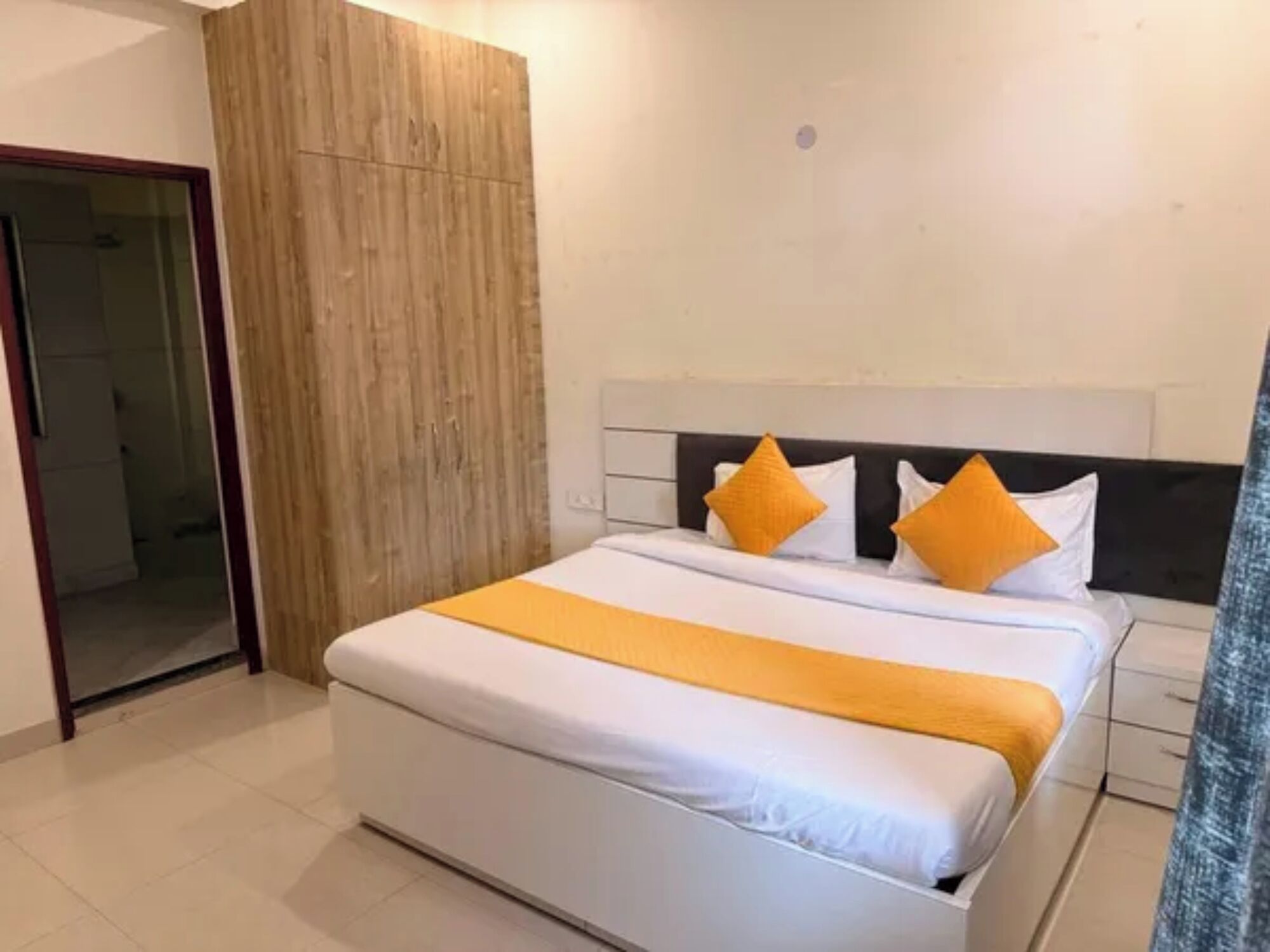 A hotel room with a bed, a wooden wardrobe, and a bathroom visible through an open door.