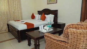 A hotel room with a bed, a wooden nightstand, a coffee table, and a wicker armchair. - Fabhotel Aravali Residency (Gurugram)