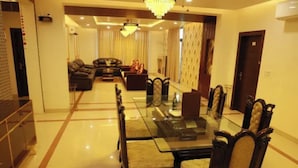 A dining area with a glass-top table and upholstered chairs, a sofa, and a chandelier. - Fabhotel Aravali Residency (Gurugram)