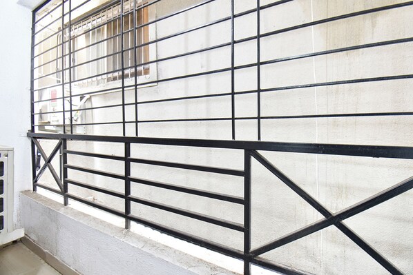 Una verja metálica con diseño de cuadrícula, un muro de hormigón y una ventana con rejas.