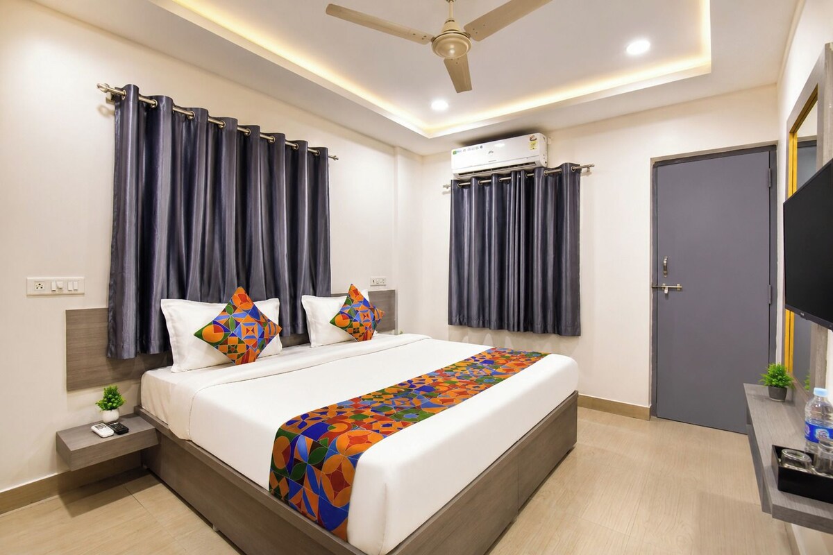 A modern hotel room with a bed, curtains, an air conditioning unit, a television, and a small plant.