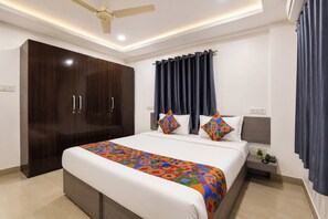 A hotel room with a large bed, a wardrobe, a bedside table with a lamp, and a ceiling fan.
