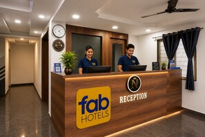 A reception desk with two staff members, a clock, and a sign for Fab Hotels.